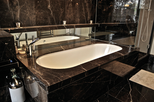 Marble bath surround with shelf passing through glass into the shower area, mirror backsplash